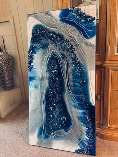 an abstract painting in blue and white on a wall next to a cabinet with drawers