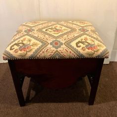 a footstool with a quilted seat cover sitting on the floor in front of a white wall