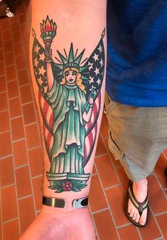 a person with a tattoo on their arm holding an american flag and the statue of liberty