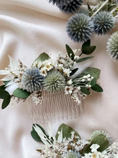 two combs with flowers and greenery on top of a white cloth covered table