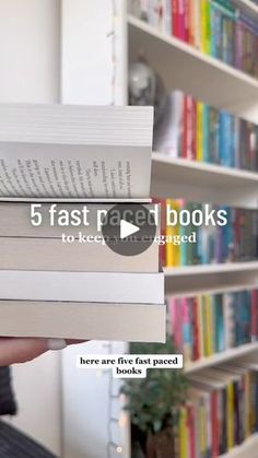 a person is holding some books in front of a book shelf with many books on it