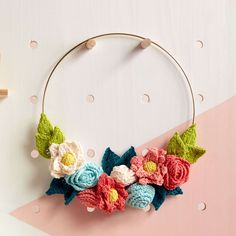 a crocheted flower wreath hanging on a pink and white wall next to wooden pegs