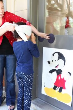 a woman standing next to a little boy near a mickey mouse drawing on a wall