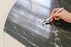 a person holding a pair of scissors on top of a black marble table with silver veining