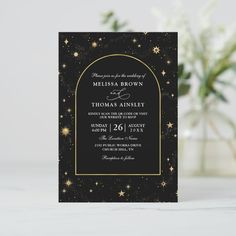 a black and gold wedding card with stars in the sky, on top of a table