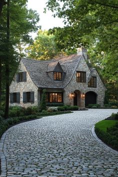 a stone driveway leading to a large brick house in the middle of a wooded area