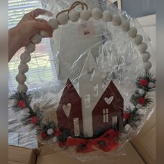 a christmas wreath with a house on it and decorations around the edges is wrapped in plastic