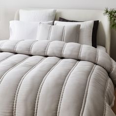 a bed with white comforters and pillows on it's side, next to a potted plant