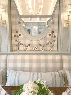 a table with flowers on it in front of a mirror and wall sconces