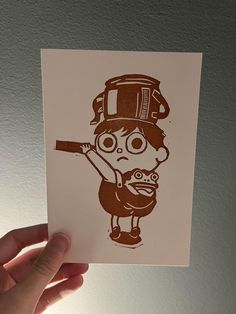 a hand holding up a card with a drawing of a person wearing a hat and holding a baseball bat