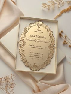 an ornate wedding card with gold foil on it and satin fabric around it, surrounded by dried flowers