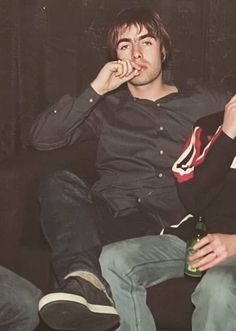 two young men sitting on a couch eating food and drinking beer while looking at the camera