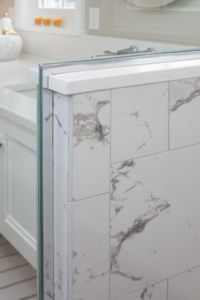 a white bathroom with marble tile on the walls and floor, along with a large mirror