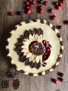 a pie decorated with chocolate and cranberries on top of a wooden table next to cookies