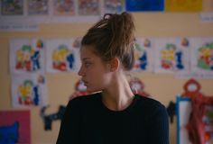 a young woman standing in front of a wall with pictures on it and looking off to the side