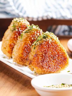 three fried food items sit on a plate next to two small bowls with dipping sauces