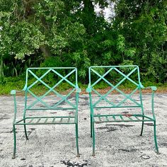 two green metal chairs sitting in the middle of a parking lot next to some trees