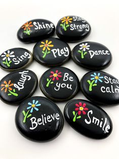 six black rocks with painted flowers and words on them that say, be you smile