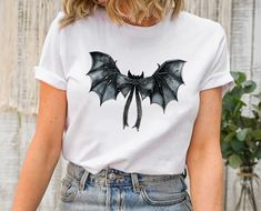 Halloween Bat Shirt, Black Bat Bow Tee , Cute Halloween Bow Tee, Spooky Gothic Bow, Halloween Women Shirt, V neck TShirt Gift Hi , I'm Eliza. Welcome to my shop! Your precious shirt is here. As a small business owner making happy  my customers with their purchase is my priority. I prepare all my shirts with love. Please don't hesitate to contact me if you have any question ,concern ,compliment or just to say hi:) Thanks for supporting me. Please check all details about your order below! BRANDS: Punk Halloween Cosplay Tops, Punk Style Tops For Halloween Cosplay, Punk Tops For Halloween Cosplay, White Halloween Cosplay Top, White Top For Halloween Cosplay, Gothic Crew Neck Top For Cosplay, Grunge Halloween Cosplay T-shirt, Edgy Halloween Cosplay T-shirt, Halloween Cosplay Short Sleeve T-shirt