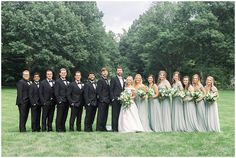 a large group of people in formal wear posing for a photo on the grass with trees in the background