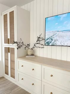 a television mounted on the wall above a white dresser with drawers and vases in front of it