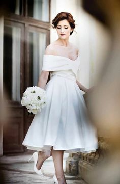 a woman in a white dress is walking down the street with her bouquet on her hand