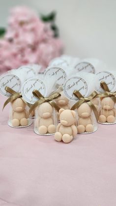 several small teddy bears in clear bags on a pink tablecloth with flowers behind them