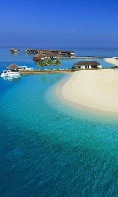 an island in the middle of blue water with houses on it and boats floating around