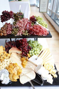 three tiered trays filled with different types of cheese and meat on top of a table