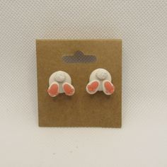 two white and pink bunny ears are on a brown card next to a pair of earrings