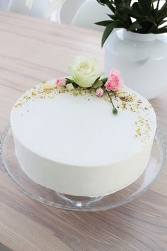 a cake with white frosting and pink flowers on top sits on a glass plate