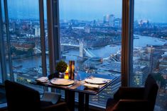 a table set for two in front of a large window overlooking the london skyline at night