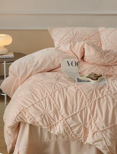 a bed with pink comforter and pillows on top of it, next to a lamp