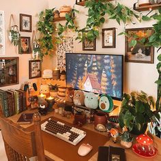 a computer desk with many plants and pictures on the wall