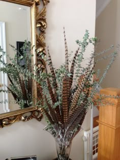 a vase filled with lots of green plants on top of a table next to a mirror