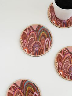 three coasters with colorful designs on them next to a coffee cup and saucer