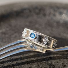 two wedding rings sitting on top of a fork with blue stones in the middle and silver filigrees