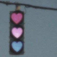 a traffic light with three hearts painted on it's back lights are red, blue, and pink