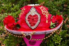 Red cowgirl hat with beaded red, gold and black heart on the front. Red lace all around, with gold accents and lots of red flowers filling the back. Around the brim is white lace, gold beaded strings, a red heart pendant and star beads. Red Brimmed Costume Hat For Festival, Red Brimmed Costume Hats And Headpieces For Festivals, Red Brimmed Festival Costume Hats And Headpieces, Red Curved Brim Costume Hat For Festivals, Red Costume Hat With Curved Brim For Festival, Red Brimmed Festival Costume Hat, Red High Crown Hat For Festival, Red Cowgirl Hat, Red Heart Pendant