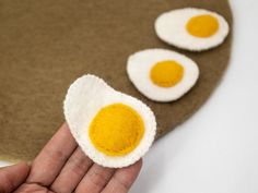 three fried eggs are placed on top of a felt piece, which is held in the palm of someone's hand