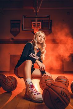 a young woman sitting on top of a basketball court next to some hoops and balls