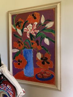 a blue vase filled with flowers on top of a table next to a wall hanging