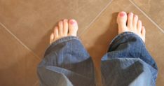 a person's feet with pink nail polish standing on a tile floor