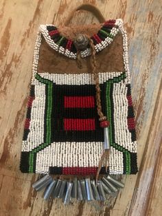 This is a beaded smoked brain tanned leather strike a light bag, in a brown colour, with beadwork in czech seed beads in white, blue , green, black, and red - and other bead embellishment.  It measures approximately 4.25" wide by 5.5" high, with 1" cones on the fringe across the bottom.  The bag is also fully lined in period fabric.  It has a leather strap on it so it can be worn on your belt, and a pewter button.    Handmade in USA! Unique Beaded Bags For Everyday Use, Unique Beaded Everyday Bags, Traditional Green Beaded Bag, Traditional Green Beaded Bags, Artisan Beaded Rectangular Bag, Artisan Brown Beaded Bag, Artisan Multicolor Beaded Bags, Traditional Beaded Rectangular Shoulder Bag, Traditional Brown Beaded Bag