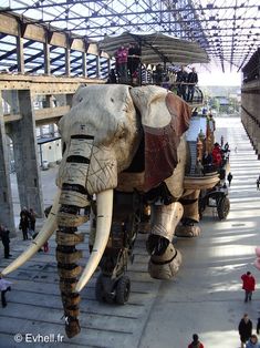 an elephant made out of wood and leather with people standing around in front of it