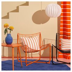 two chairs and a table with flowers on it in front of an orange striped wall