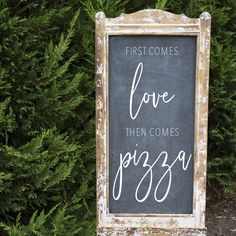 a chalkboard sign that says, first comes love then comes pizza in front of some bushes