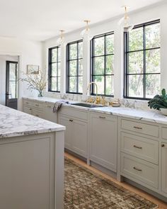 a kitchen with white cabinets and marble counter tops, along with an area rug on the floor