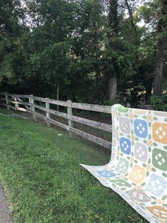 a patchwork quilt draped over a wooden fence in the grass next to a road