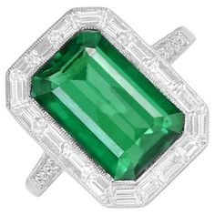 This striking ring showcases a vivid green 5.38-carat Zambian emerald at its center. Encircling the emerald is a halo of baguette-cut diamonds totaling 0.87 carats. The shoulders are adorned with micro-pave set round brilliant cut diamonds, adding approximately 0.14 carats to the overall design. Handcrafted in platinum, this ring is certified for its quality and craftsmanship. Ring Size: 6 US, Resizable Metal: Platinum Stone: Diamond, Emerald Stone Cut: Emerald Cut Style: Art Deco Total Weight: 7.51 grams Width Of Band: 1.82 mm Green Octagon Platinum Ring, Emerald Ring With Halo Setting In Platinum, Green Emerald Ring With Halo Setting In Platinum, Green Emerald Platinum Ring With Halo Setting, Platinum Baguette Cut Green Emerald Ring, Gia Certified Green Emerald Ring In Platinum, Octagon Green Emerald Ring With Center Stone, Gia Certified Green Emerald Platinum Ring, Green Platinum Emerald Ring For May Birthstone